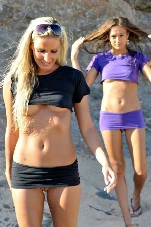 Two girls expose their underboobs and shaved pussies on a sandy beach on realgirlsweb.com